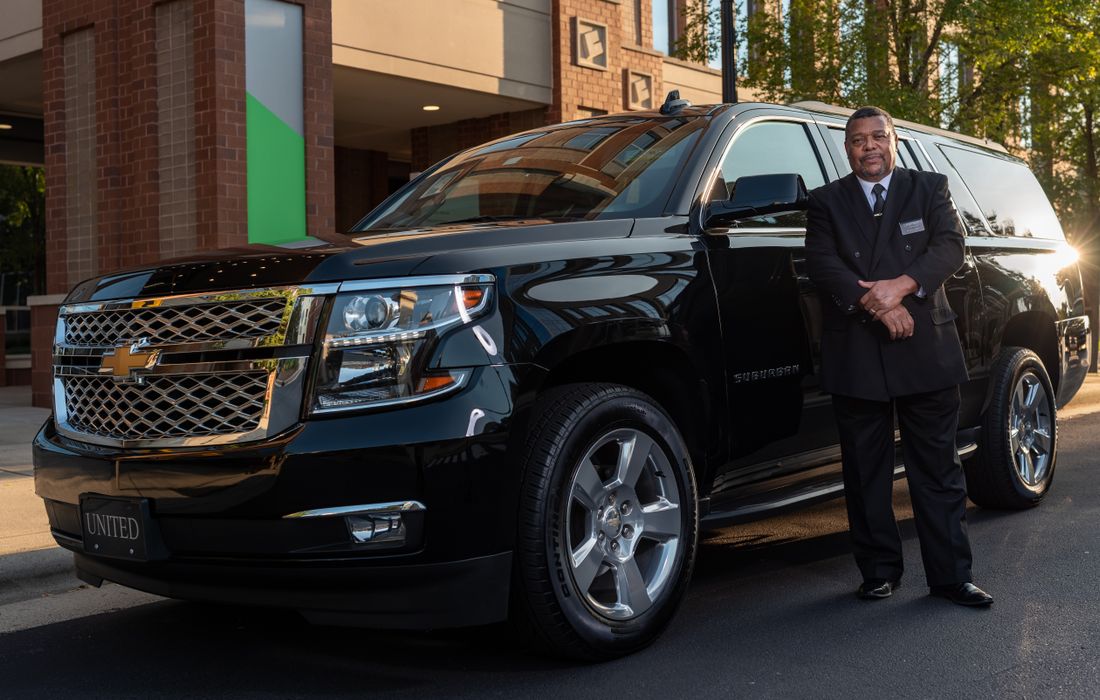 Chauffeur beside a black executive vehicle, airport transfer priced per car not per seat